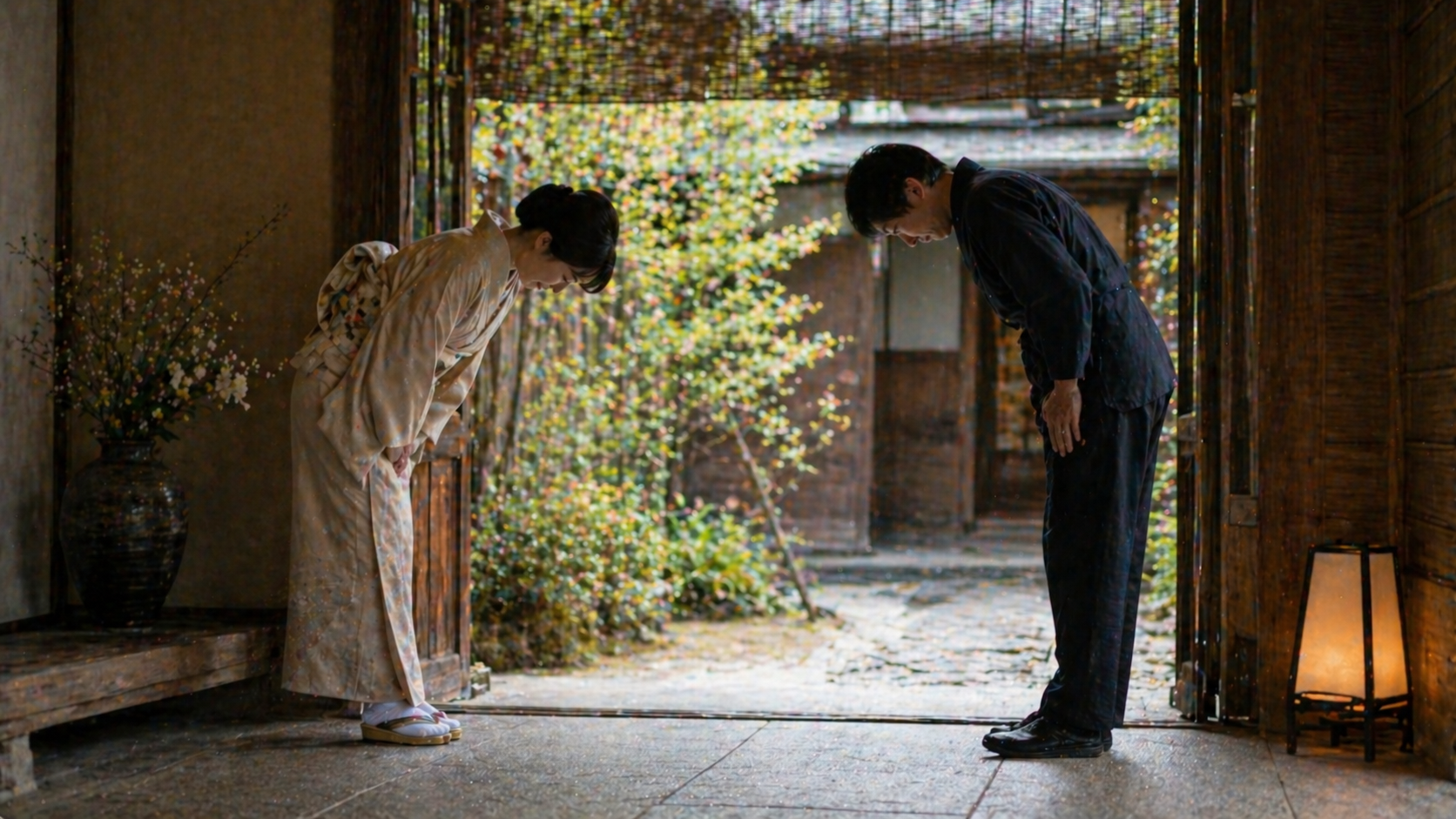 Two people bowing politely at a traditional Japanese ryokan entrance with soft natural lighting